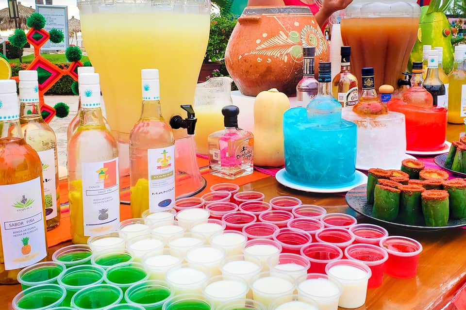 Colorful tropical drink bar display with bottles, juices, cakes, and vibrant beverages