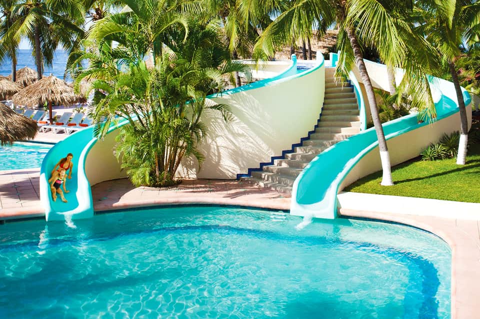 Water slide feature with turquoise accents in tropical pool setting with palm trees