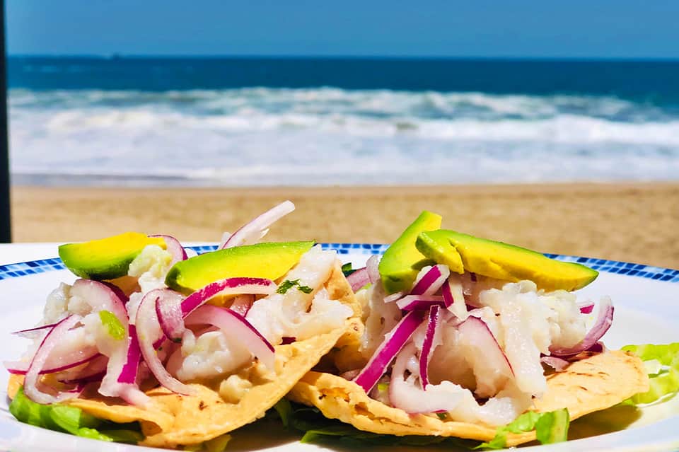 Fresh ceviche tacos with avocado and pickled onion served beachside with ocean backdrop