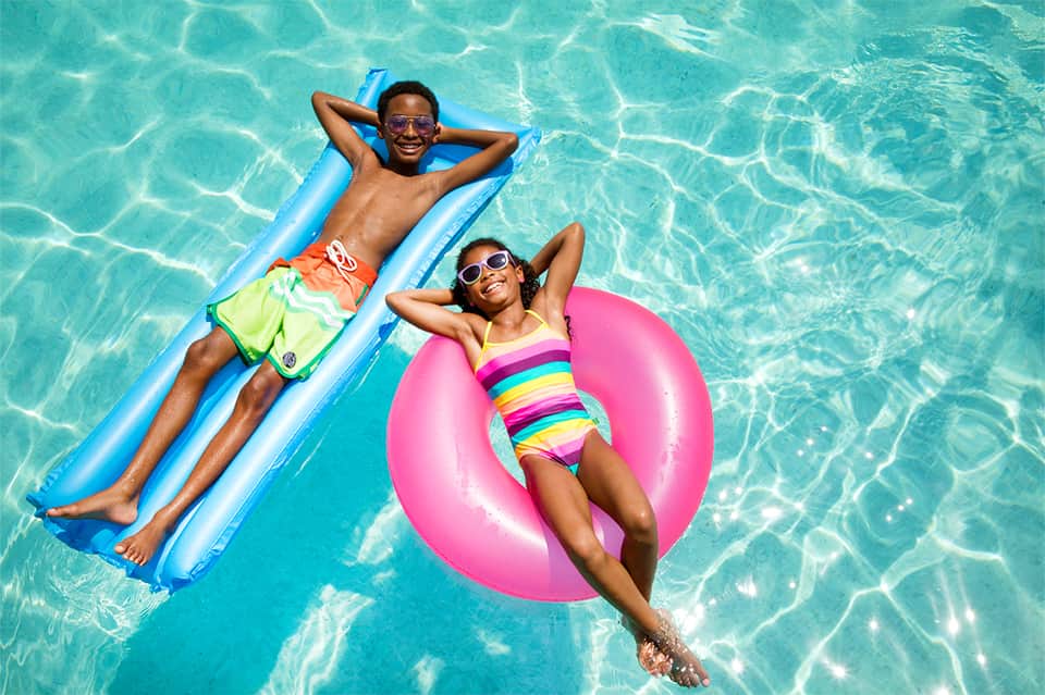 Children on colorful float toys in crystal-clear swimming pool water