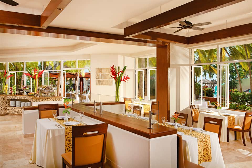Modern restaurant dining area with wood beams, tropical flowers, and ocean views
