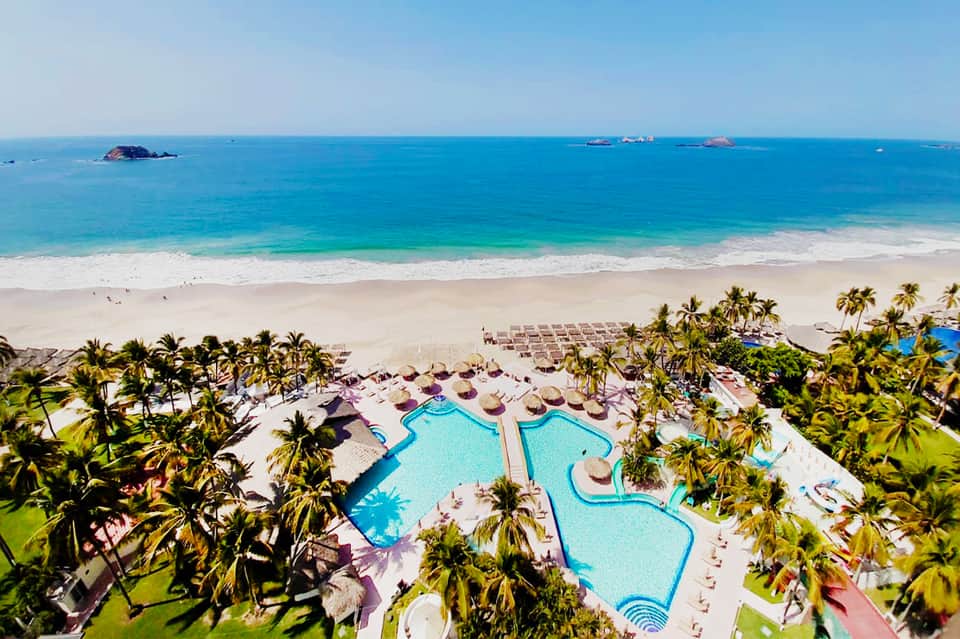 Aerial view of beachfront resort with pools and palm trees