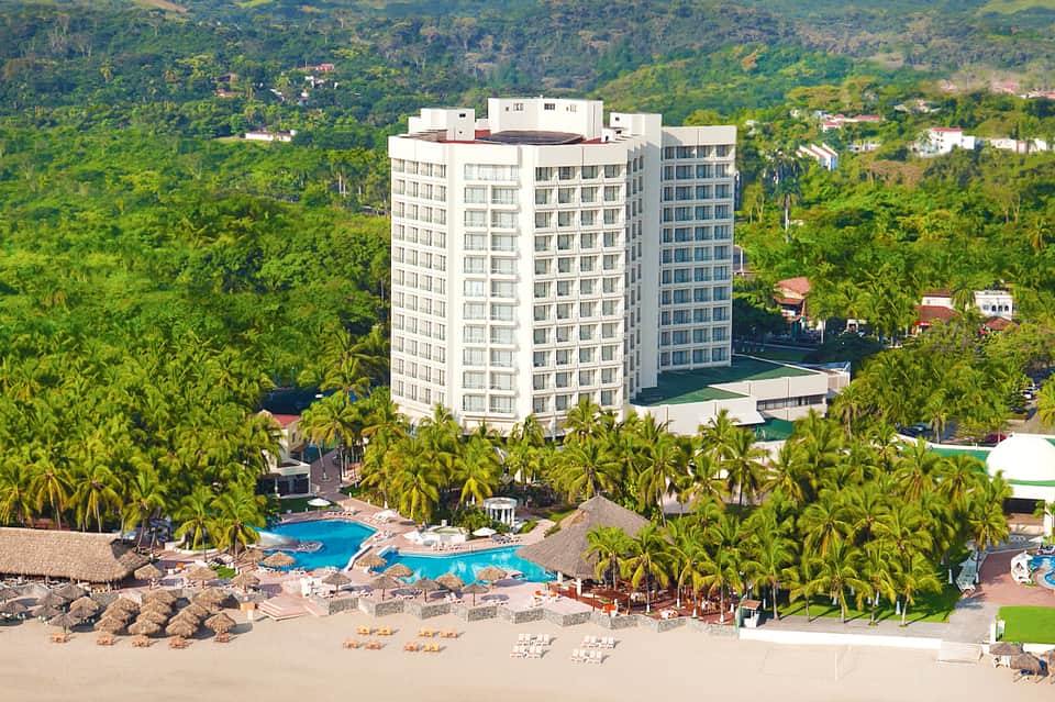 Beachfront resort hotel surrounded by tropical palm trees with multiple pools and lounge areas