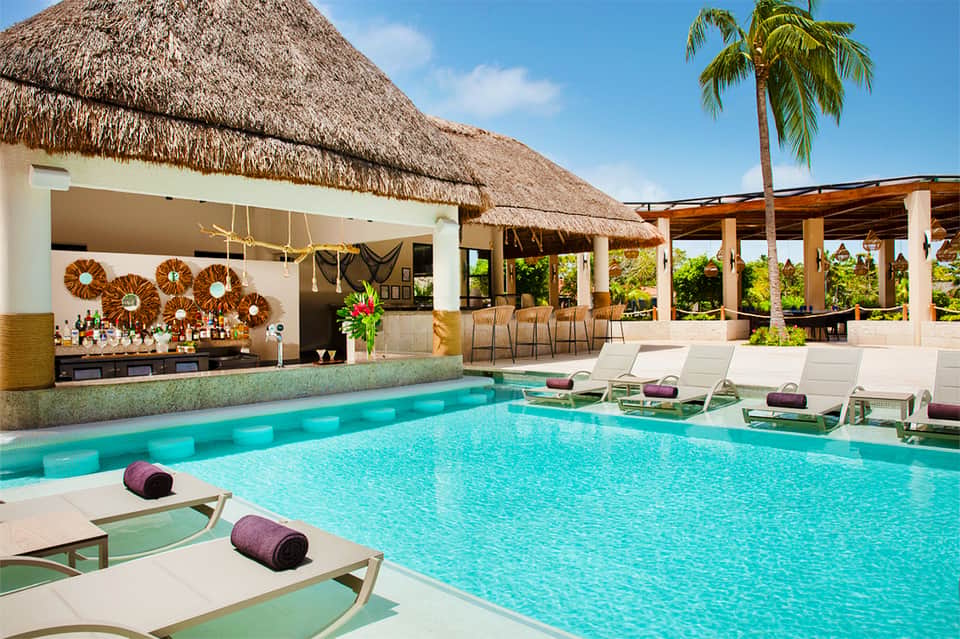 Luxury resort pool with thatched-roof bar, lounge chairs, and tropical landscaping