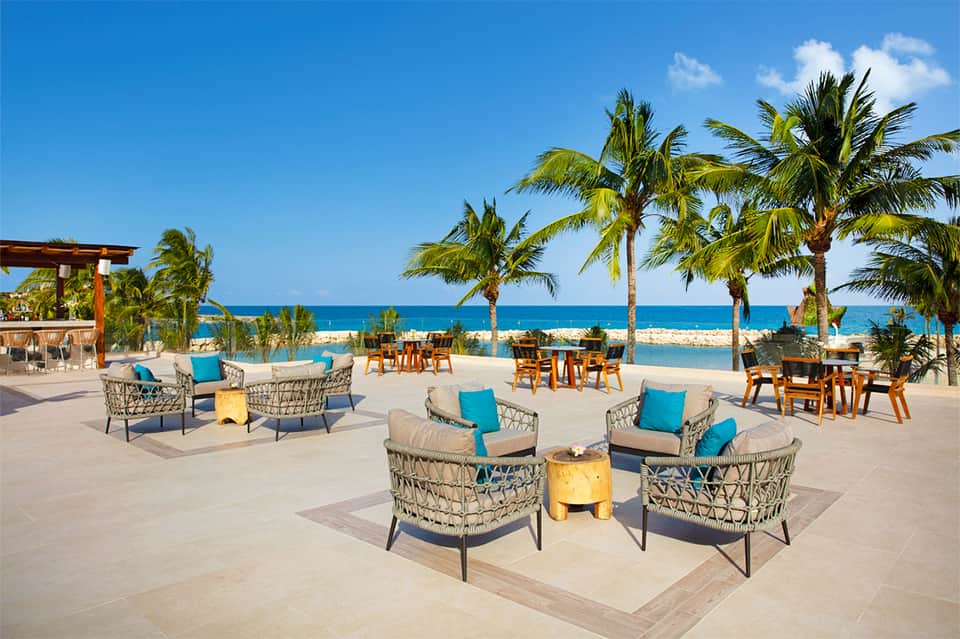Beachfront patio area with woven chairs, fire pits, and ocean view lined with palm trees