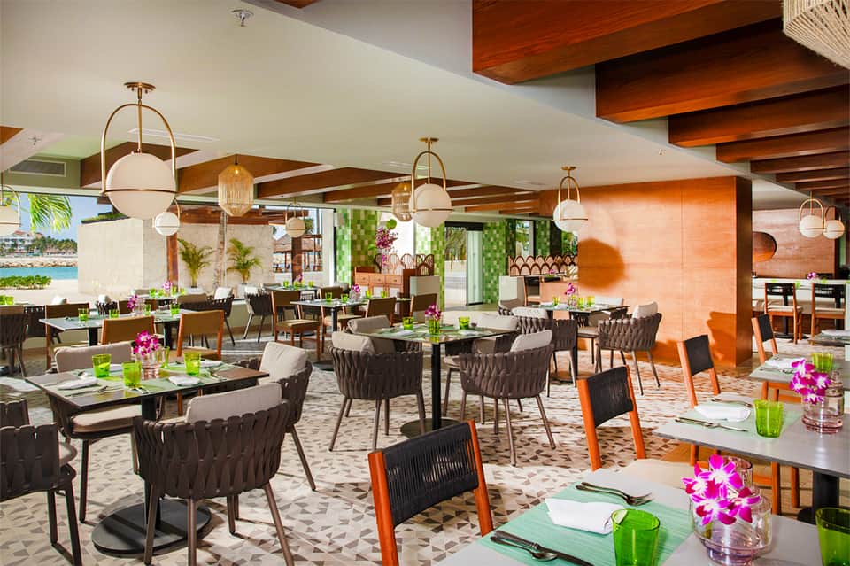 Modern resort dining area with tropical plants, pendant lighting, and colorful floral centerpieces