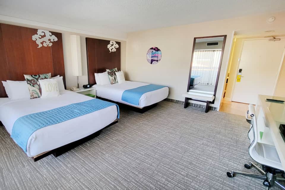 Spacious hotel room with two queen beds, brown headboards, and bright windows