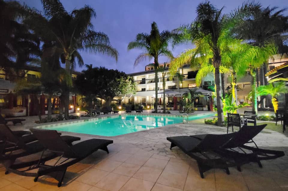 Illuminated resort courtyard pool at dusk surrounded by palm trees and loungers