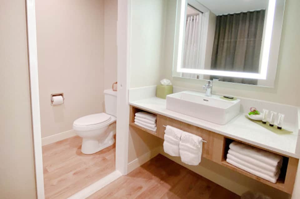 Modern hotel bathroom with white vessel sink, illuminated mirror, and wooden vanity storage