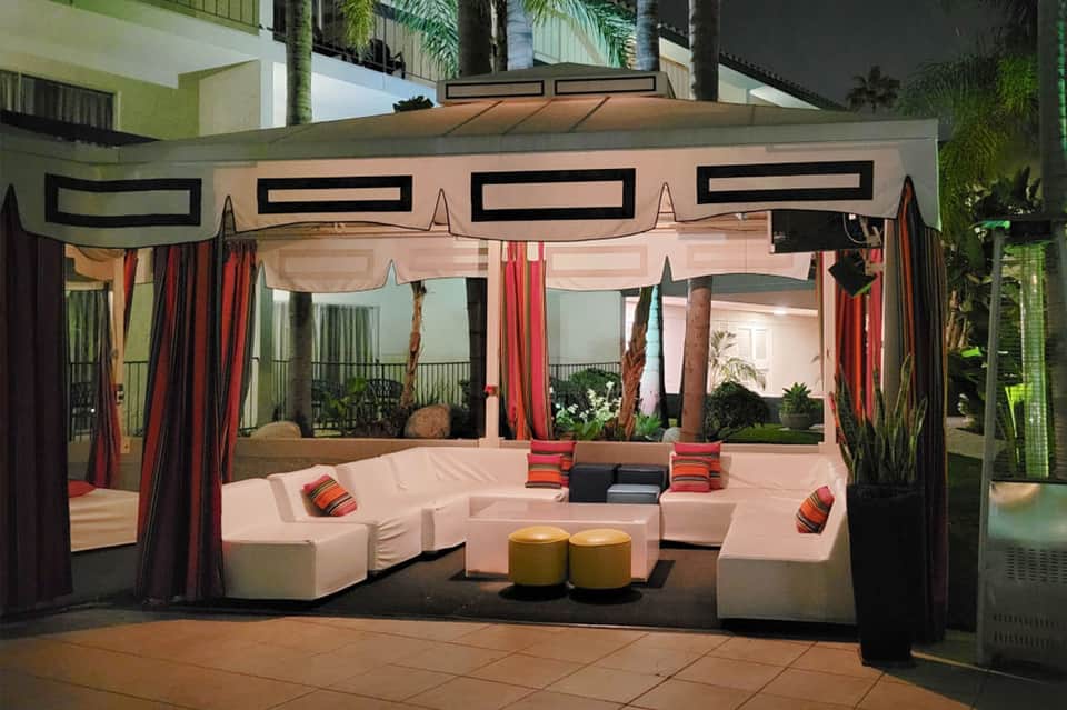 Modern lounge cabana with pink seating, red curtains, and geometric black design elements