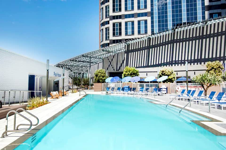 Resort swimming pool with blue lounge chairs, pergola shade structures, and high-rise building