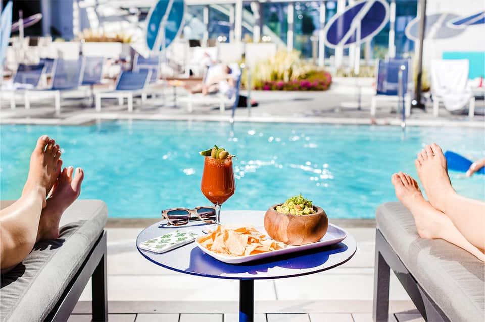 Poolside dining table with cocktail and appetizers overlooking sparkling resort swimming pool