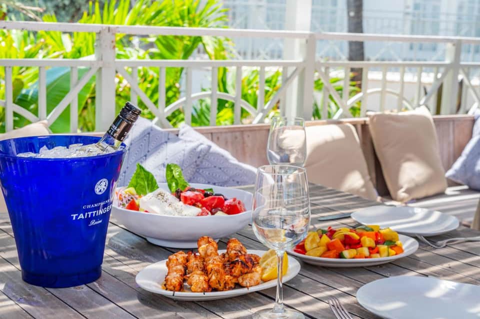 Luxury resort balcony table with champagne bucket, gourmet dishes, and city skyline view beyond railing