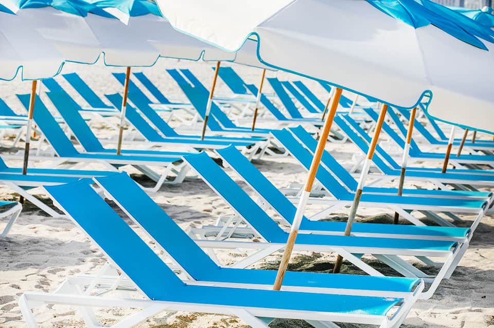 Row of blue and white striped beach lounge chairs under shade umbrellas
