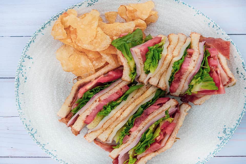 Gourmet bacon and lettuce sandwich with potato chips on decorative white plate