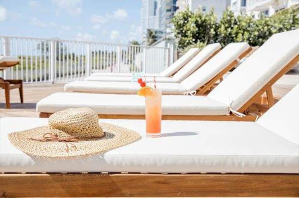 Beachfront lounge chairs with umbrella and refreshment on sunny deck with ocean view