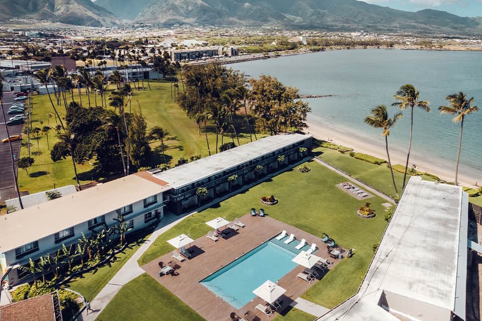 Aerial view of beachfront resort pool with loungers overlooking bay and mountains