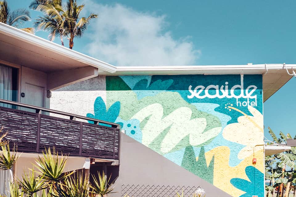 Seaside hotel exterior with colorful mural featuring tropical flowers and palm trees