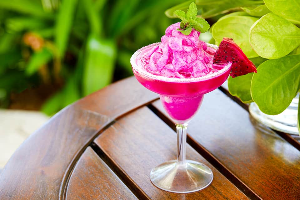 Vibrant pink frozen margarita cocktail with salt rim, garnished with lime and surrounded by foliage