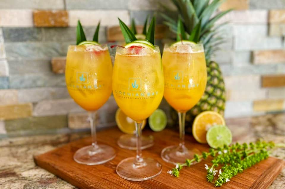 Three tropical cocktails in tall glasses garnished with pineapple leaves on wooden serving board