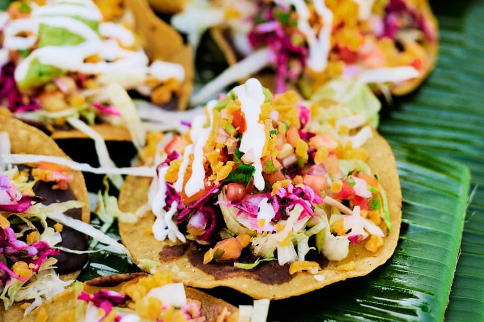 Colorful tacos topped with vibrant pink cabbage and white sauce on a banana leaf
