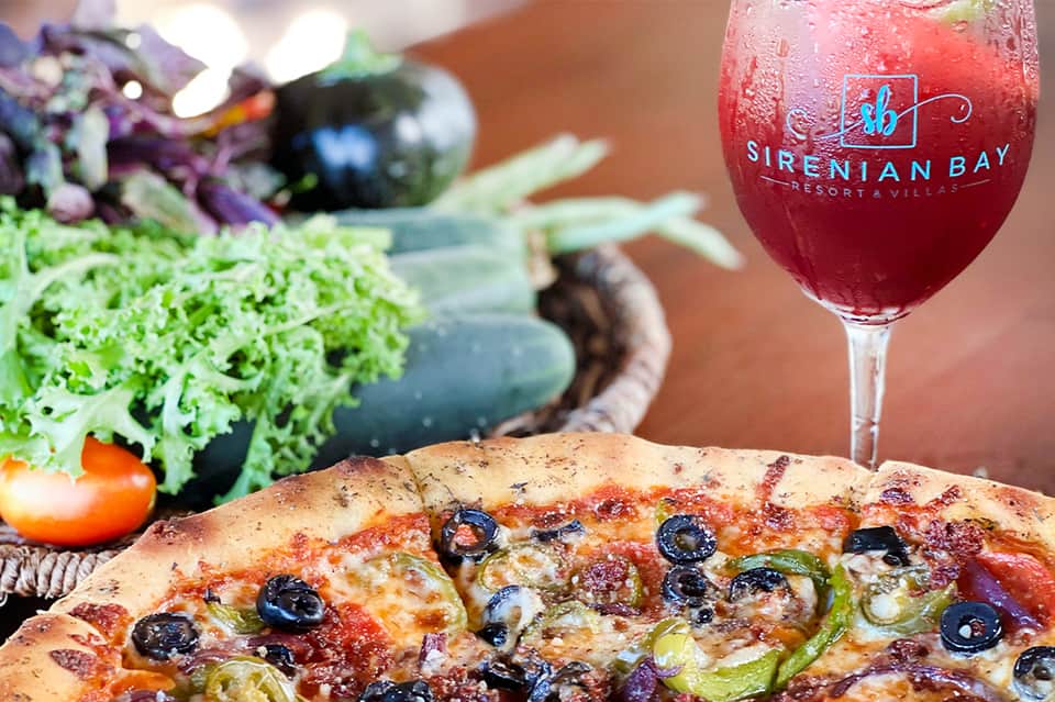 Gourmet pizza and wine glass branded with Sirenian Bay at an upscale resort