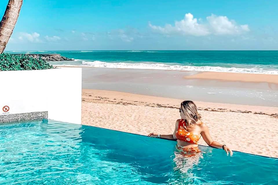 Woman in infinity pool overlooking tropical beach with turquoise ocean and white sand