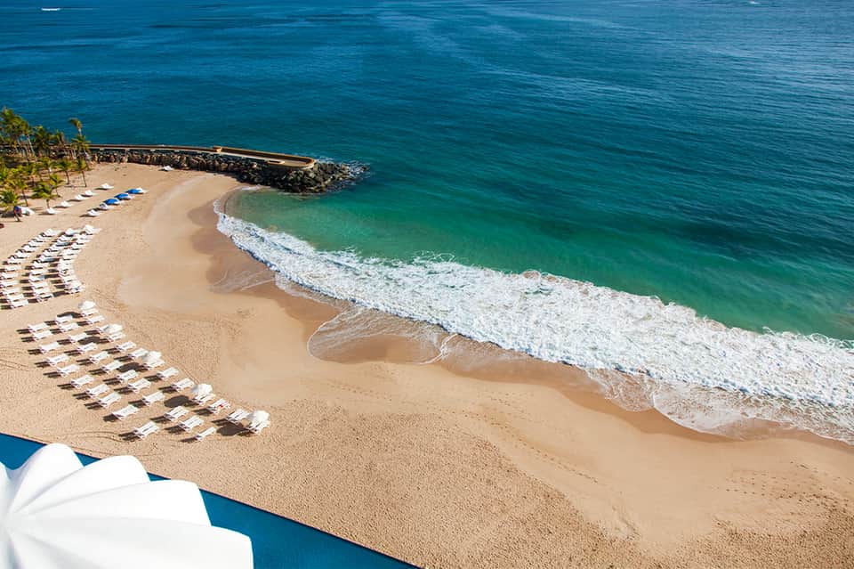 Tropical beach resort with sandy shore, turquoise ocean waves, and rows of white beach chairs