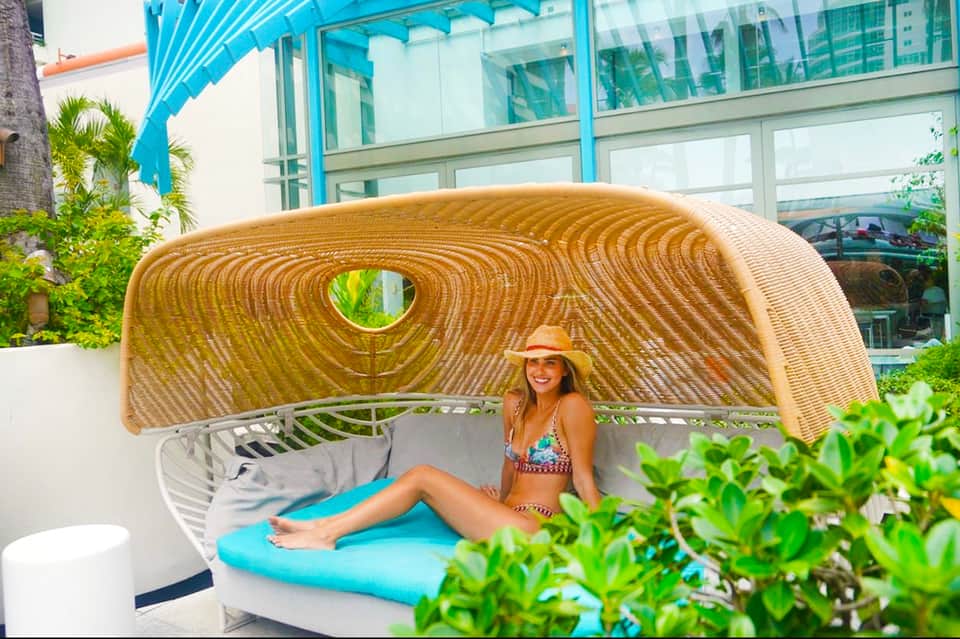 Woman in swimwear reclining in modern woven daybed with turquoise cushion