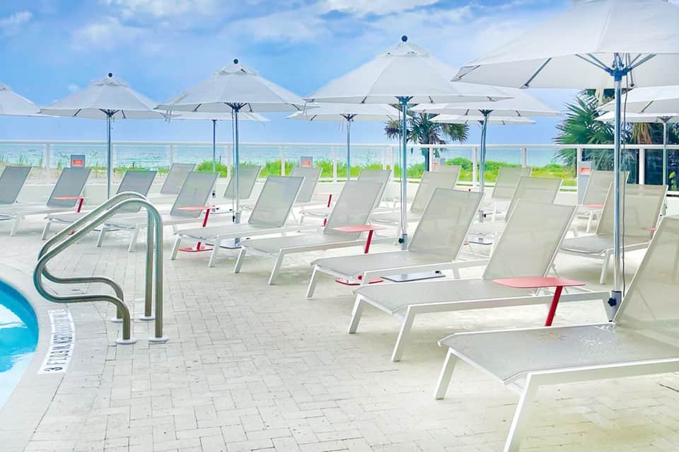 Oceanfront pool deck with white lounge chairs and umbrellas overlooking the beach and sea