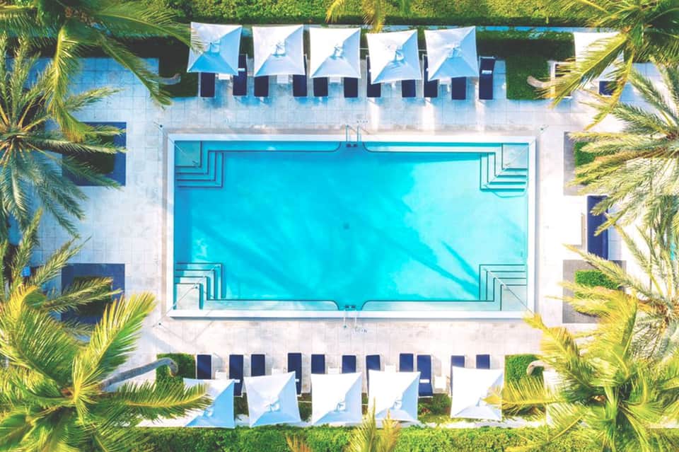 Aerial view of rectangular turquoise pool surrounded by white umbrellas and palm trees