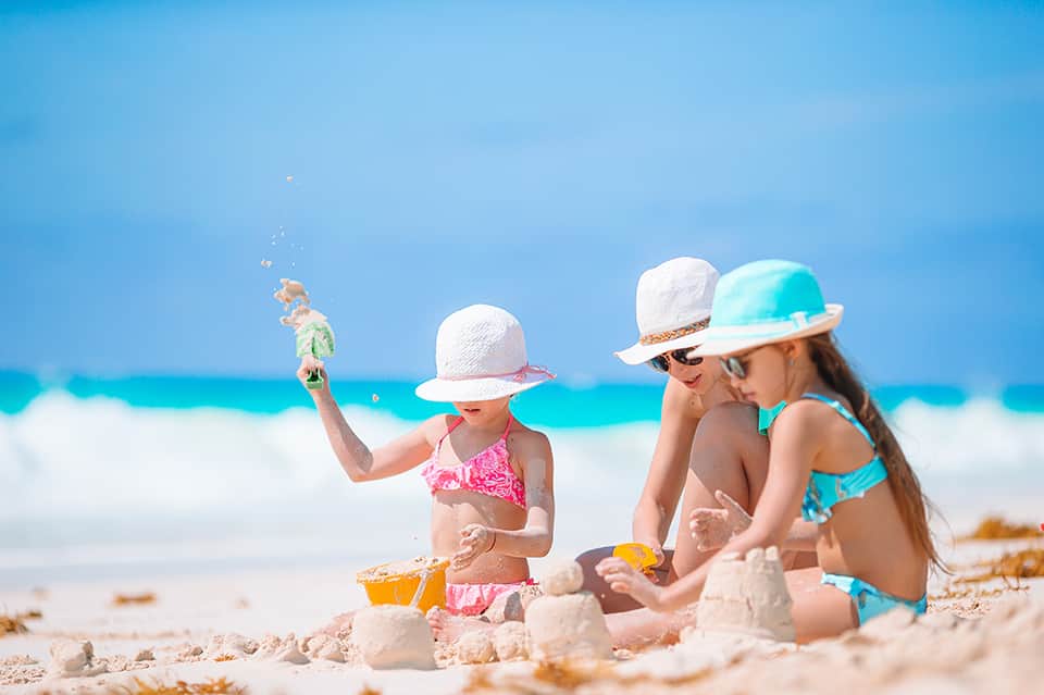 Children building sandcastles on beach wearing hats, building sand structures