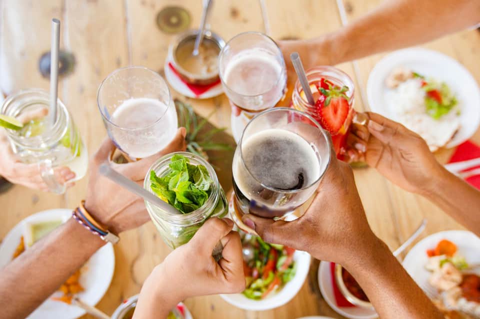 Friends toasting with drinks at a wooden table with food and place settings during daytime