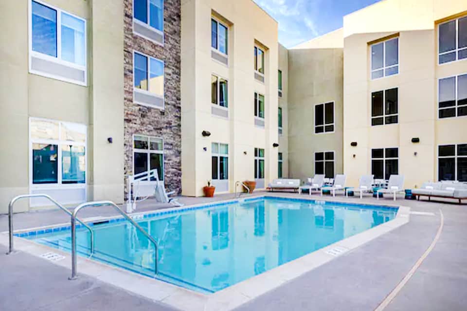 Indoor hotel pool with metal railings, white loungers, and modern building architecture