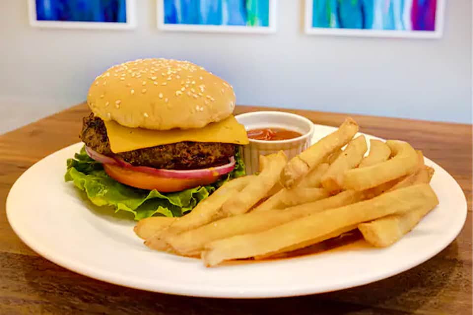 Gourmet burger with sesame bun, cheese, lettuce, tomato, and crispy fries on white plate