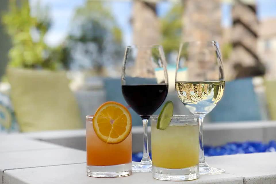Three cocktails displayed poolside: orange drink, red wine, and white wine with citrus garnish