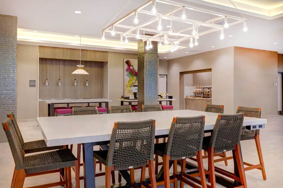 Bright meeting room with geometric pendant lighting, white table, woven chairs, and lounge seating