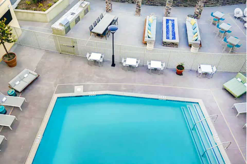 Aerial view of rectangular pool with white lounge chairs and blue umbrellas on pool deck