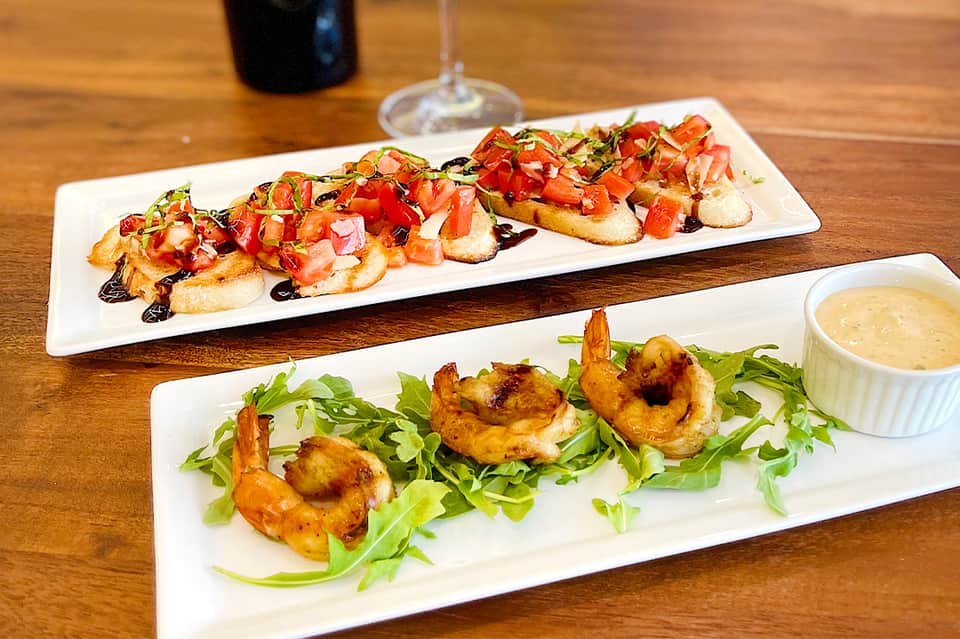 Gourmet bruschetta and shrimp appetizers with dipping sauce on wooden table