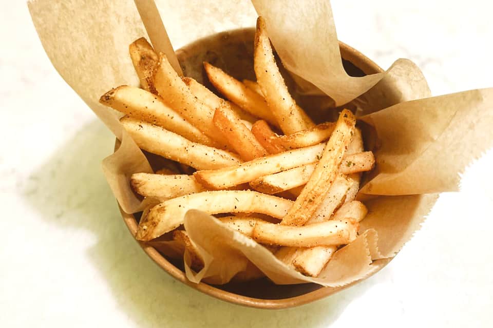 Golden crispy french fries served in a paper cone on a white background