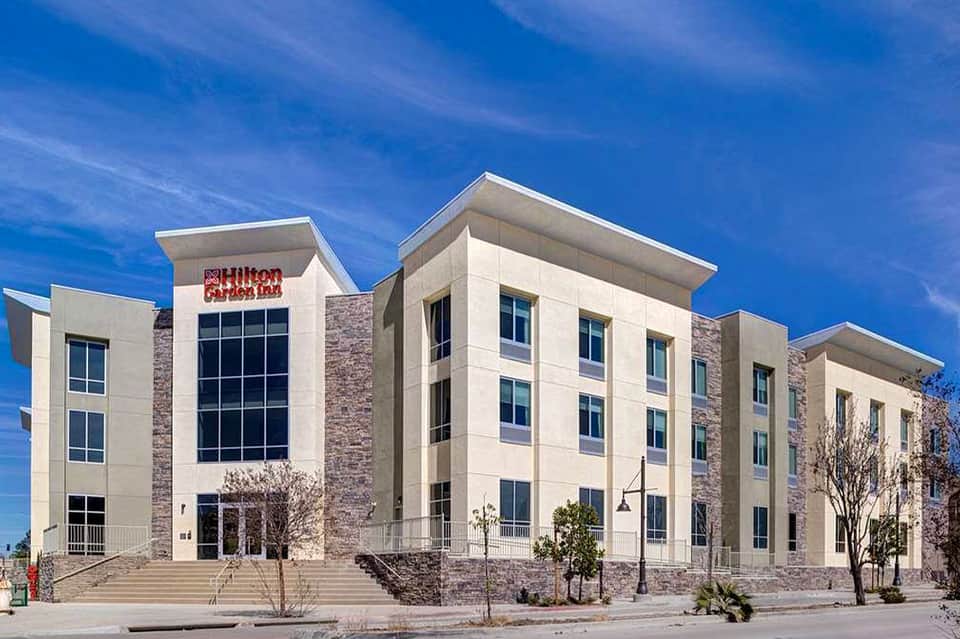 Hilton Garden Inn exterior with contemporary architecture, stone and white facade under blue sky