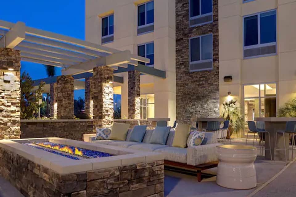 Outdoor patio at dusk with fire pit, lounge seating, stone pillars, and illuminated building facade