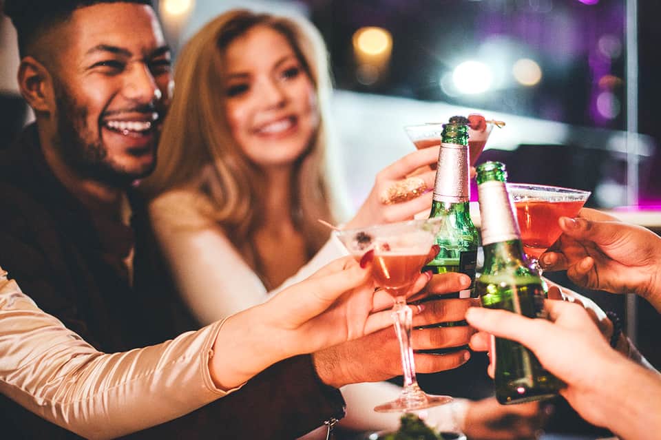 Friends toasting with beer bottles and cocktails at an evening celebration with colorful lighting