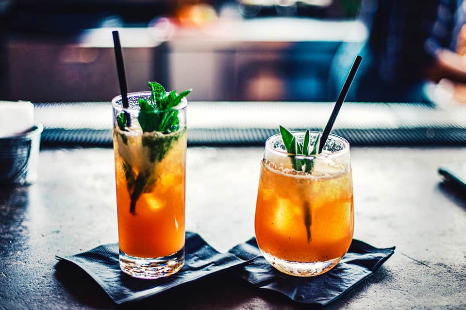 Two tropical cocktails with mint garnish and black straws on slate coasters