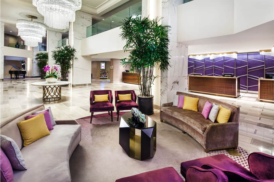 Luxury hotel lobby with marble floors, modern furniture, chandeliers, and purple accent colors