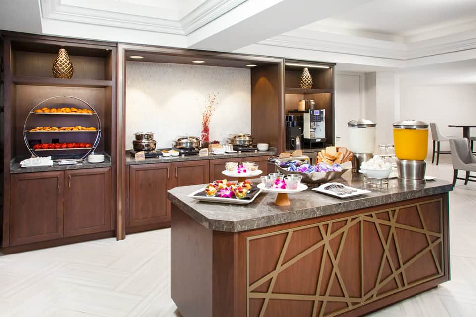 Upscale hotel breakfast buffet with pastries, fresh fruit, beverages, and elegant wood cabinetry