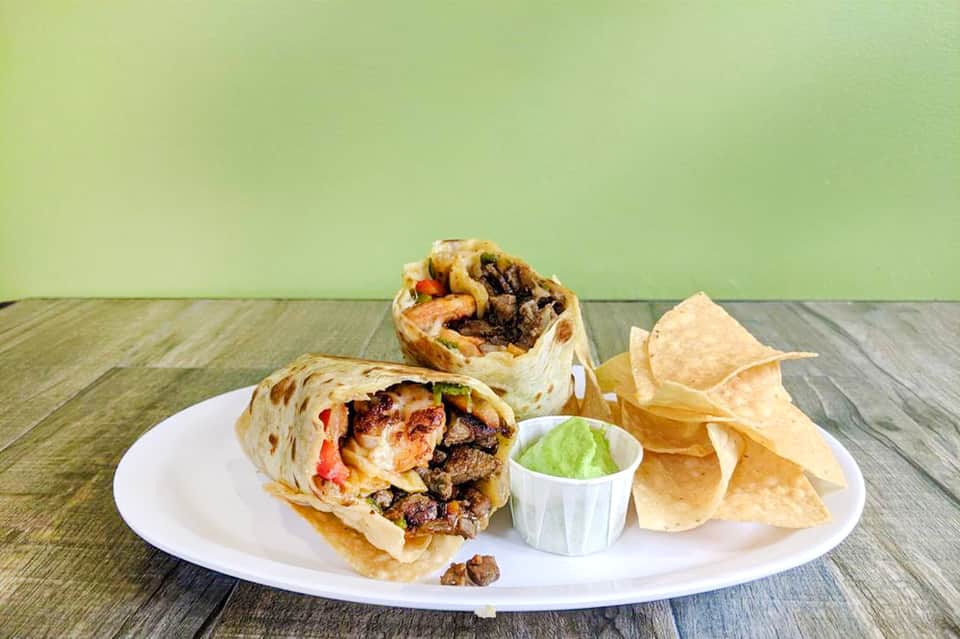 Two wrapped burritos with tortilla chips and guacamole on white plate with green wall