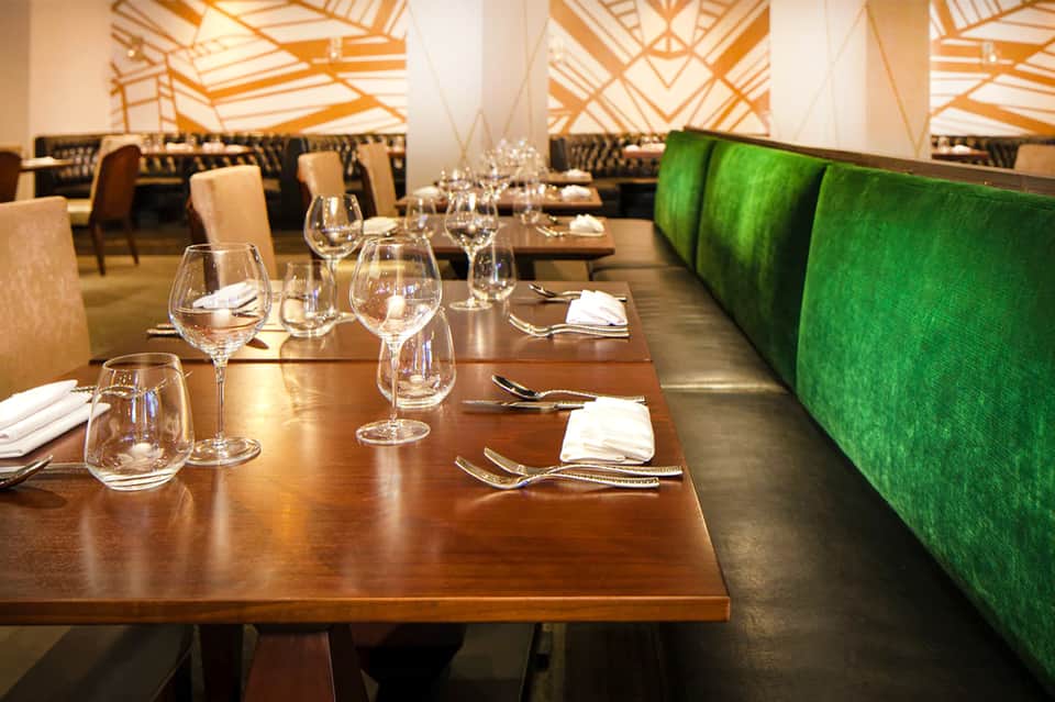 Fine dining restaurant with wooden tables, wine glasses, and geometric ceiling design