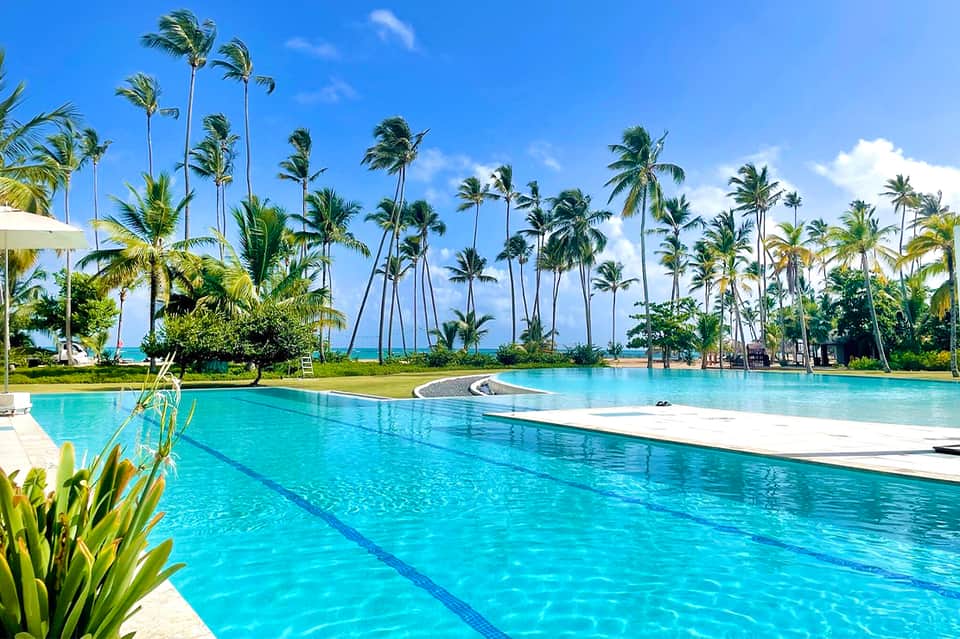 Large outdoor lap pool surrounded by palm trees with turquoise water and blue sky