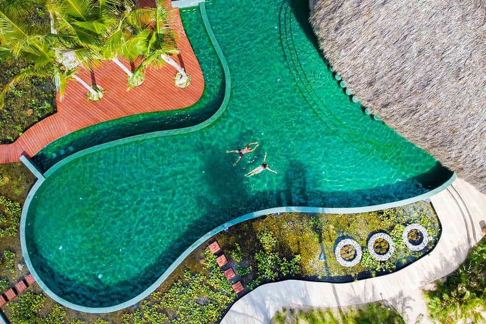 Aerial view of turquoise lagoon-style pool with swimmers and red wooden deck